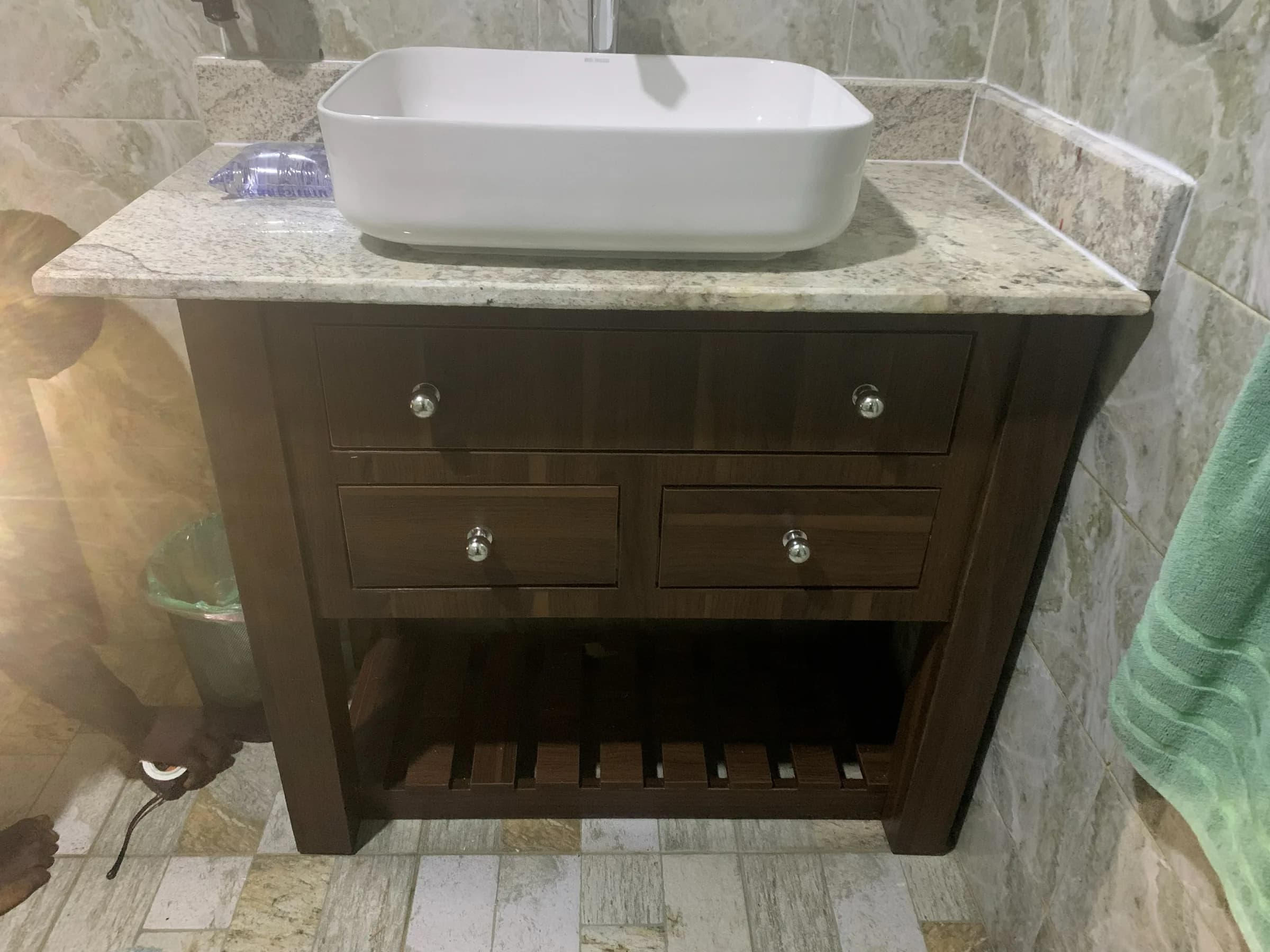 Dark timber bathroom vanity with granite top and white vessel basin against tiled wall.