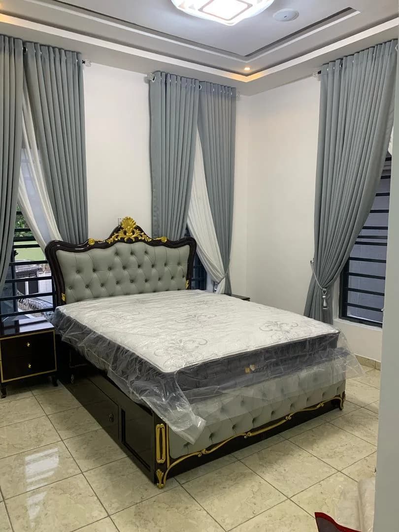 Bedroom with gilded tufted bed under a coffered ceiling, mattress wrapped in plastic.
