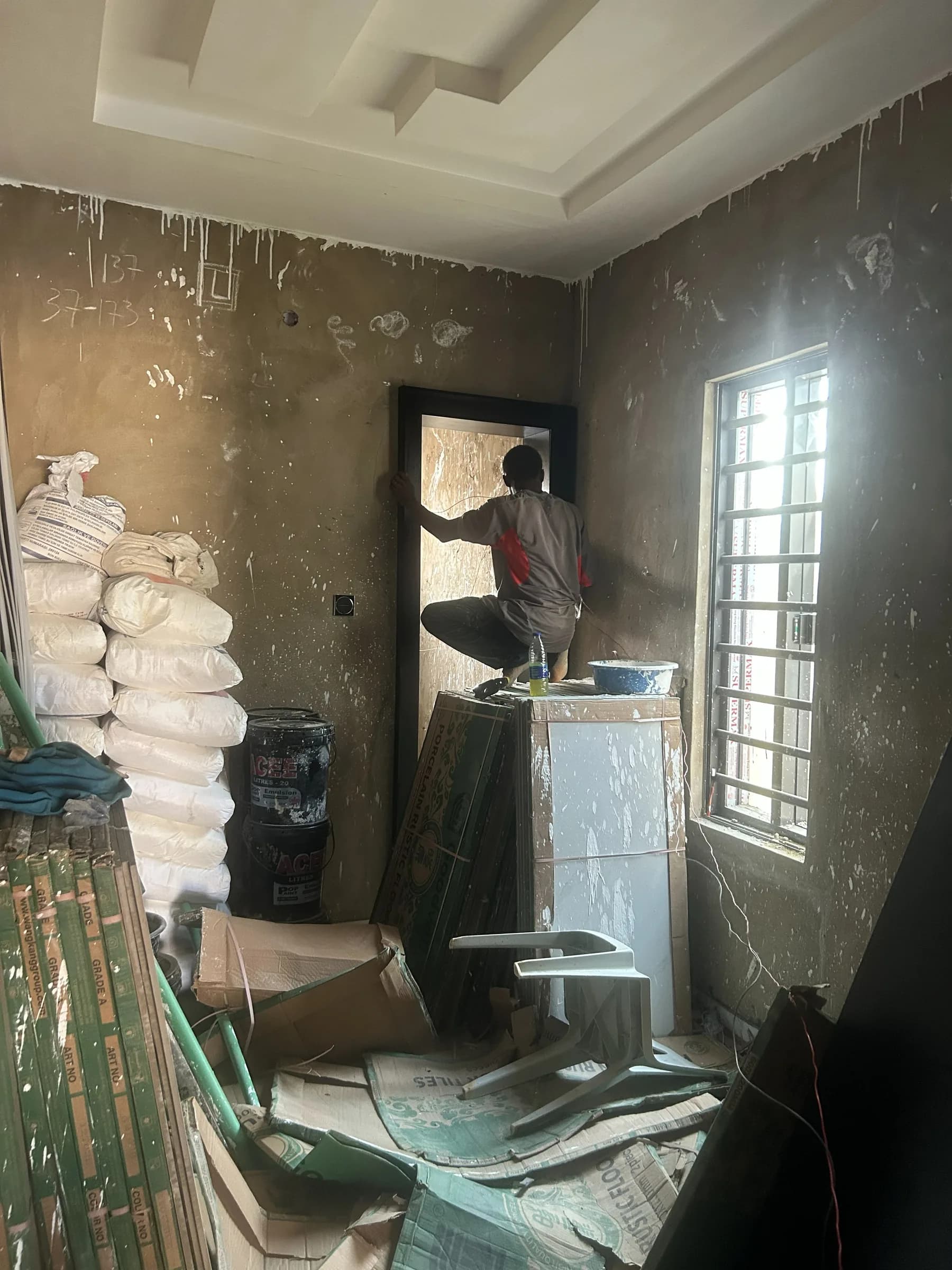 A fitter working in a doorway in a raw, unplastered room, materials stacked against the wall.