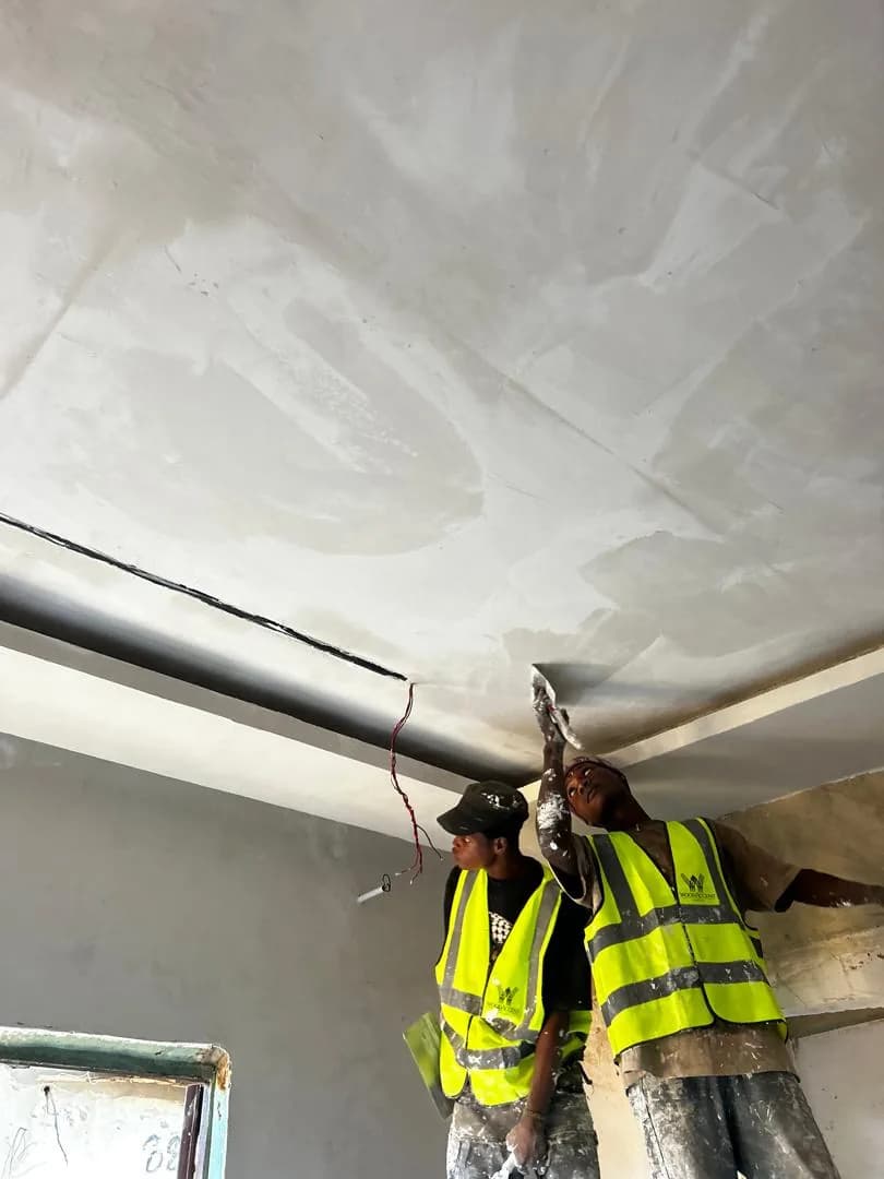 Two WoodAccent fitters in hi-vis vests working a fresh skim coat into a ceiling cove.