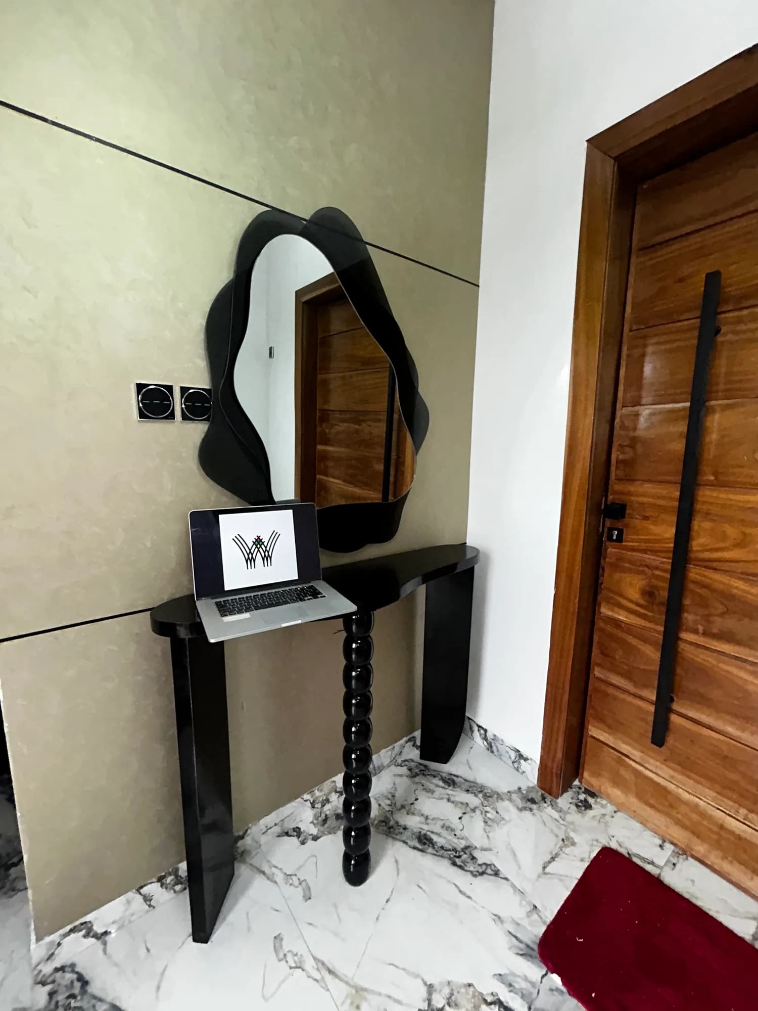 Side view of a dark console and organic-shaped mirror beside a timber door.