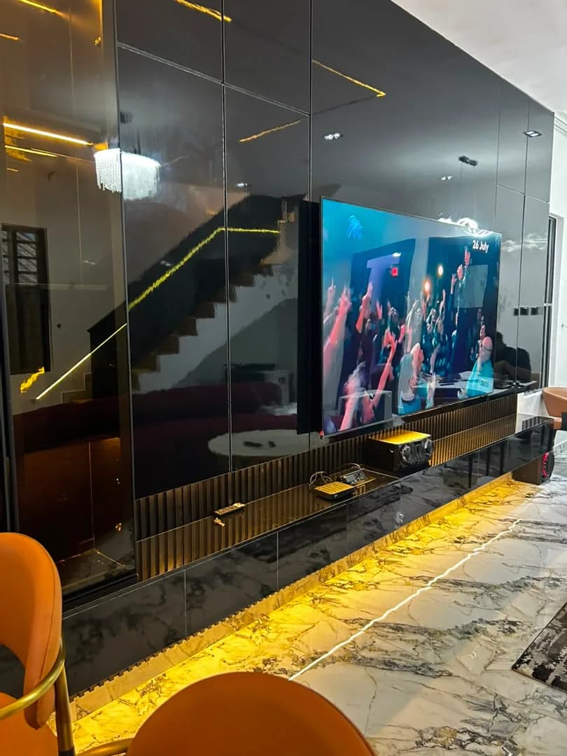 Wide view of a fluted media console beneath a wall-mounted TV set into tinted glass panelling.