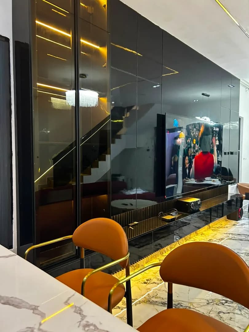 Fluted media console and tinted glass partition wall behind tan leather counter chairs.