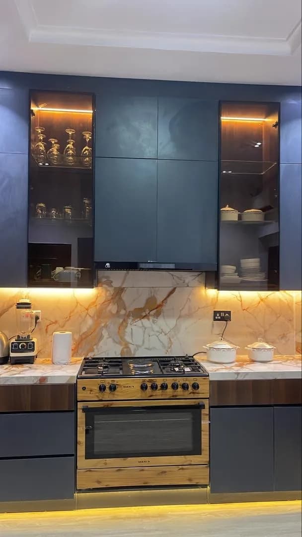 Fitted kitchen with navy cabinets, lit glass display units, marble backsplash and a freestanding gas range.