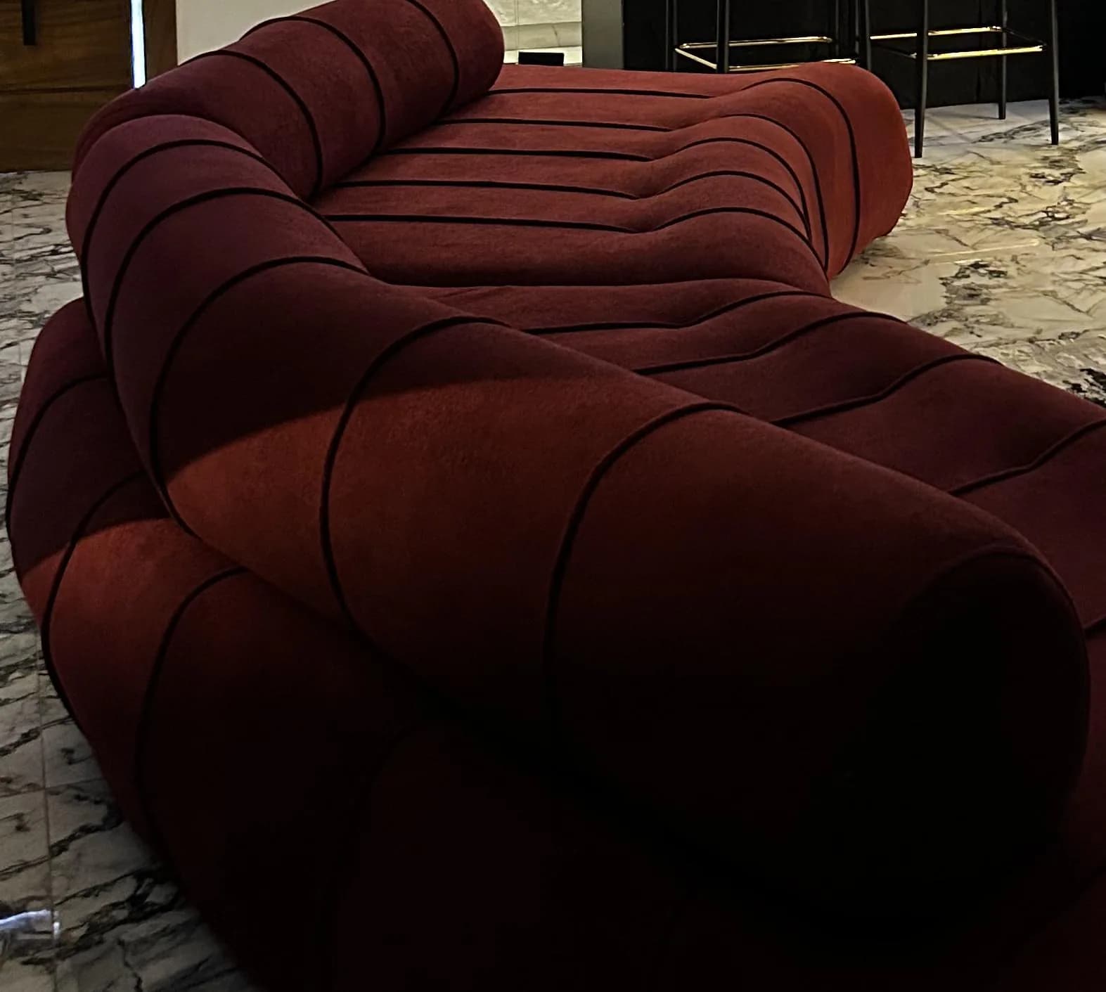 The Helix’s burgundy bolster curling over its channelled seat on veined marble