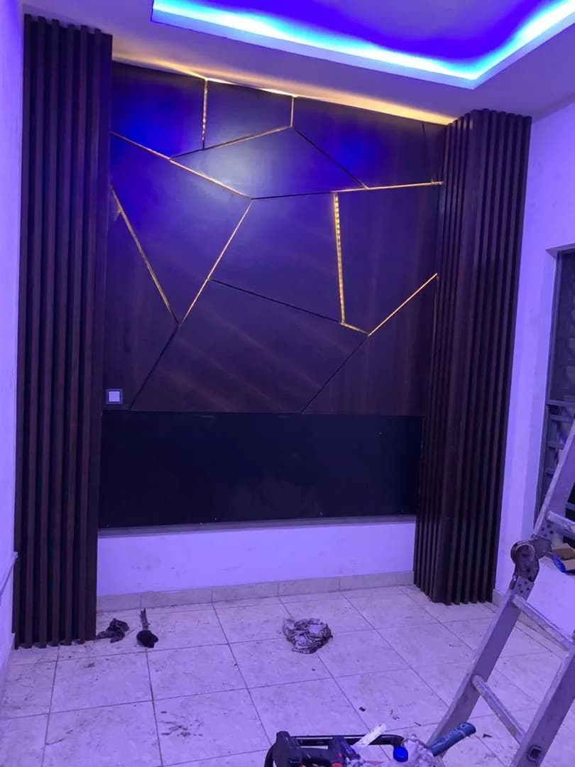 Dark timber feature wall with gold LED inlays and blue cove lighting, mid-install with a ladder and debris.