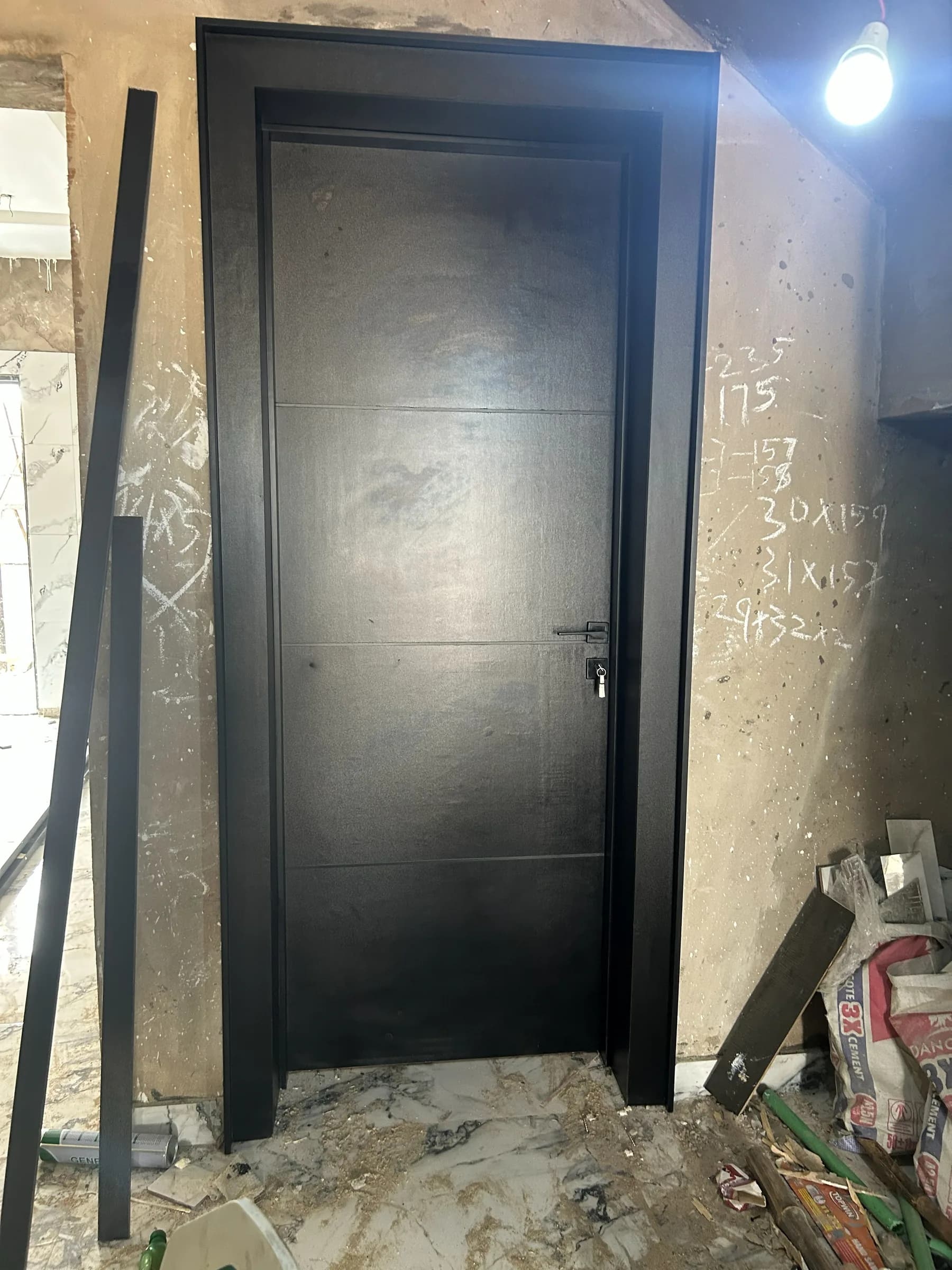 Matte black door with fine horizontal grooves hung in a black frame in a raw room.
