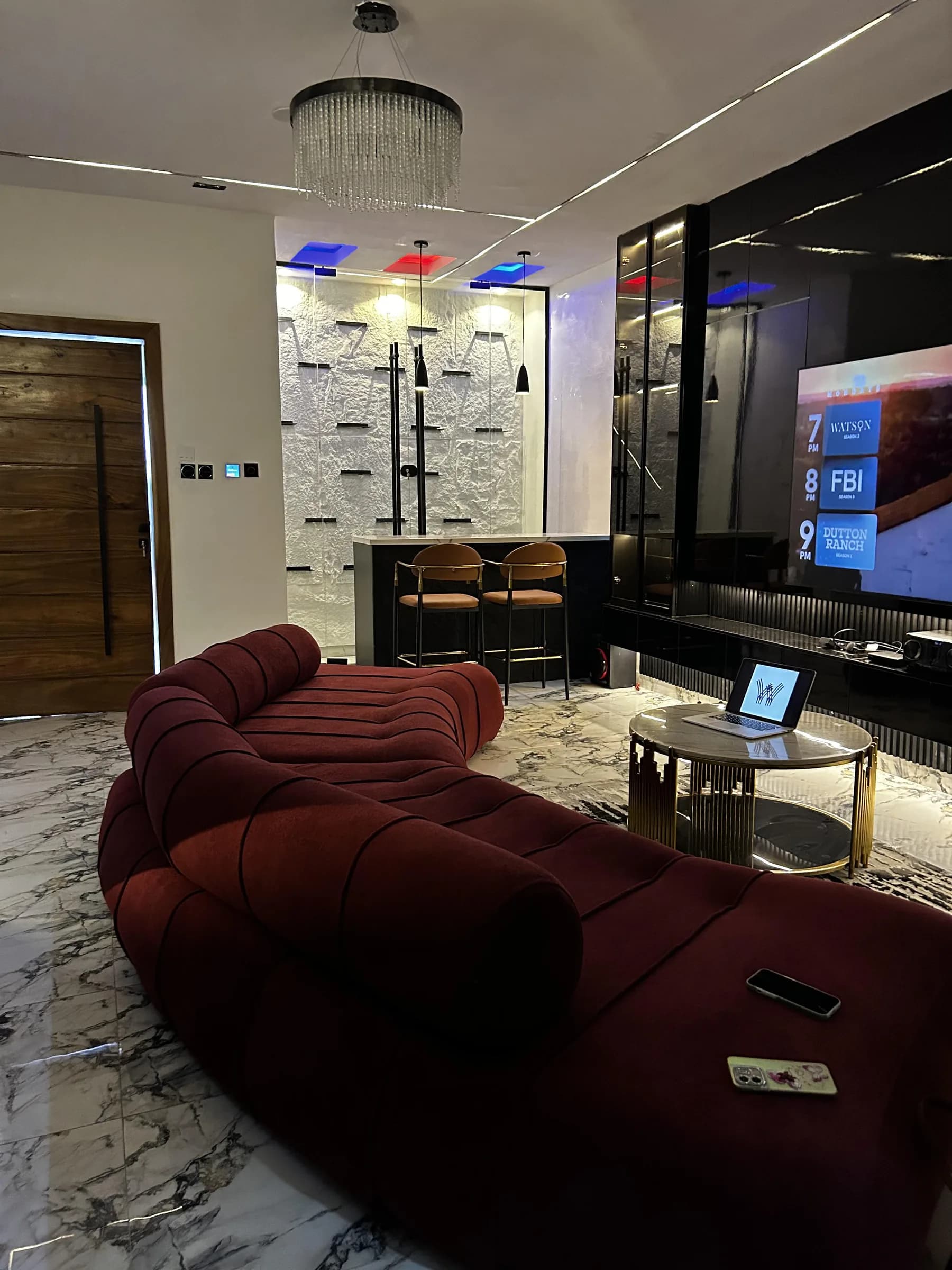 The full curve of the burgundy Helix sofa between a timber plank door, a lit bar and a brass coffee table.