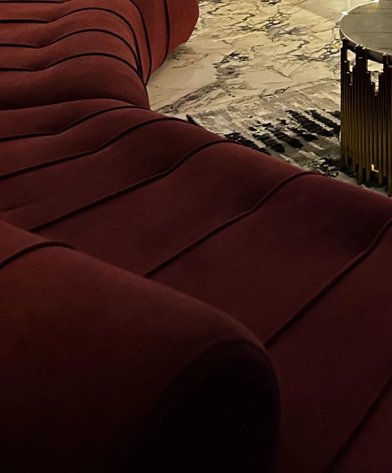 Low along the burgundy velvet channels of the Helix, a brass table at the edge of the frame.